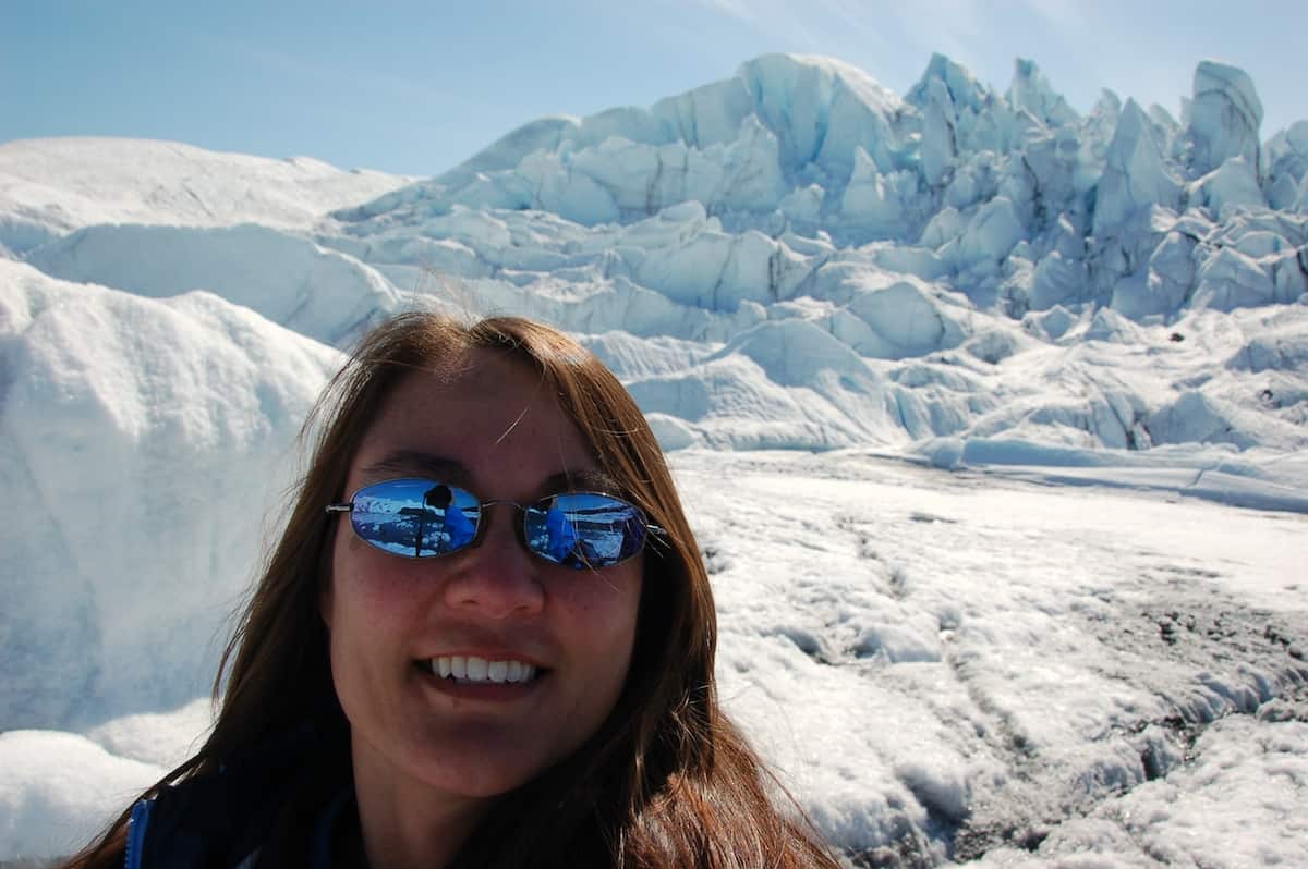 smiling brunette wearing sunglasses taking selfie at glacier field