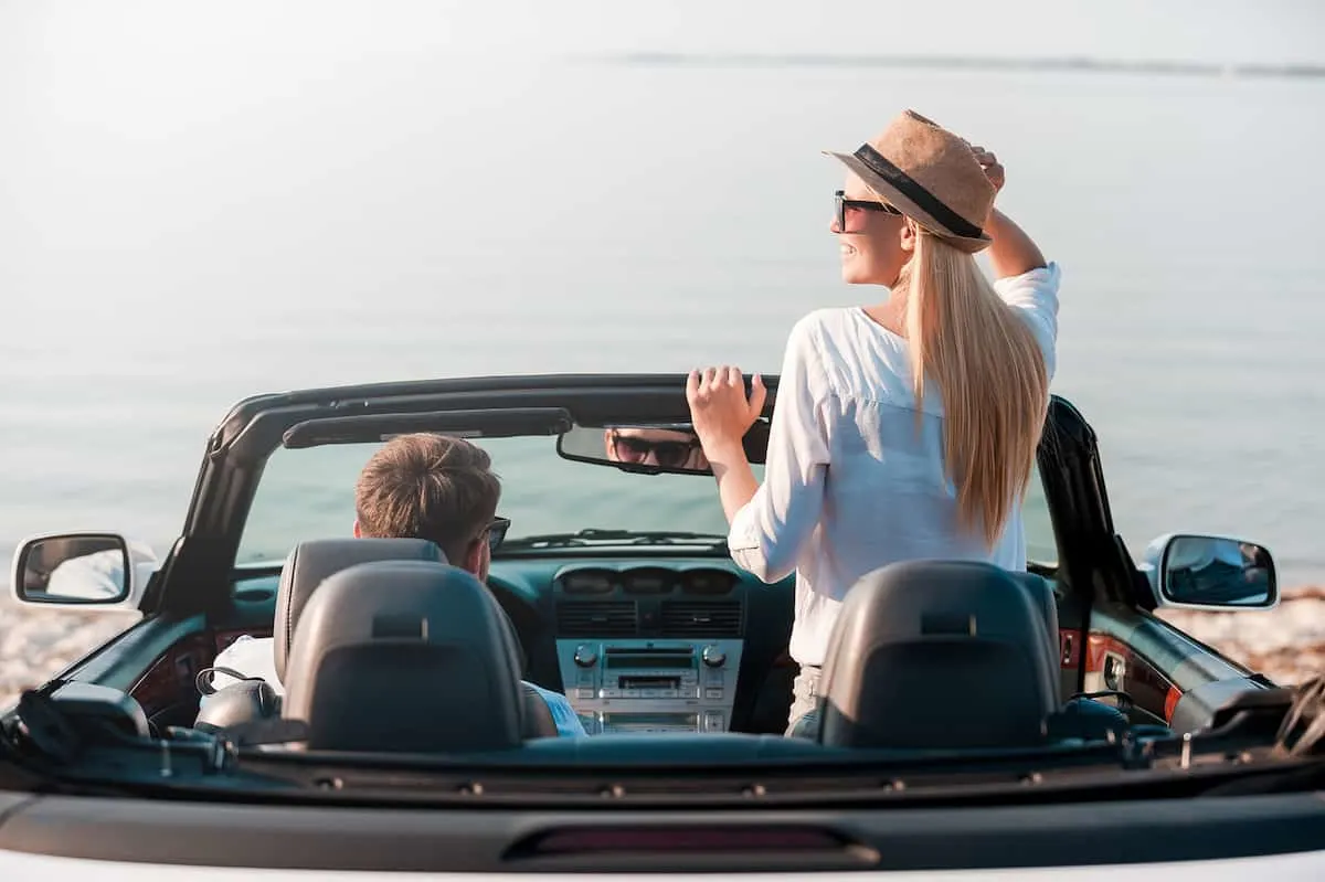 Rear view of smiling young woman enjoying scenery while her boyfriend sitting near on front seat of their convertible