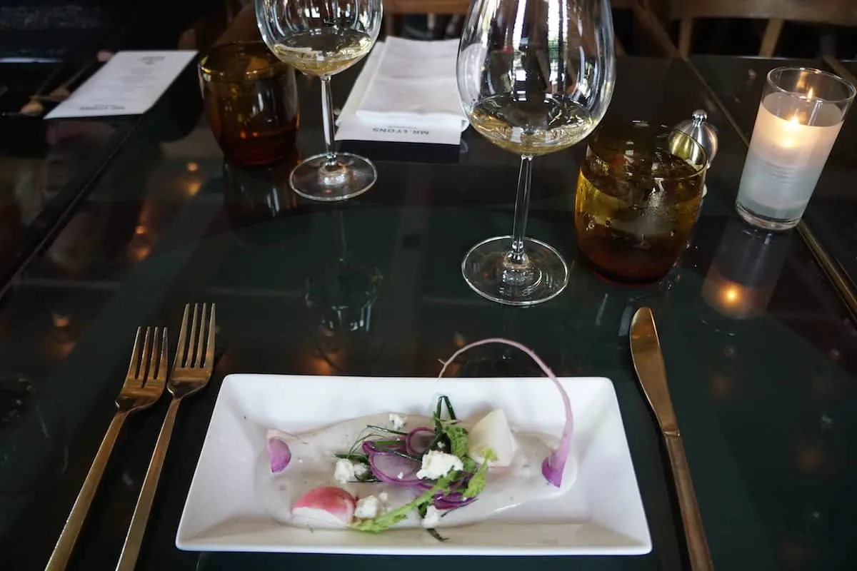 pink purple radishes in dressing on a white plate with a glass of white wine