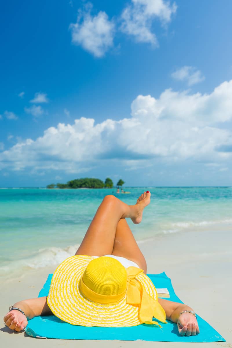 Woman lies on the beach with yellow hat and blue towel