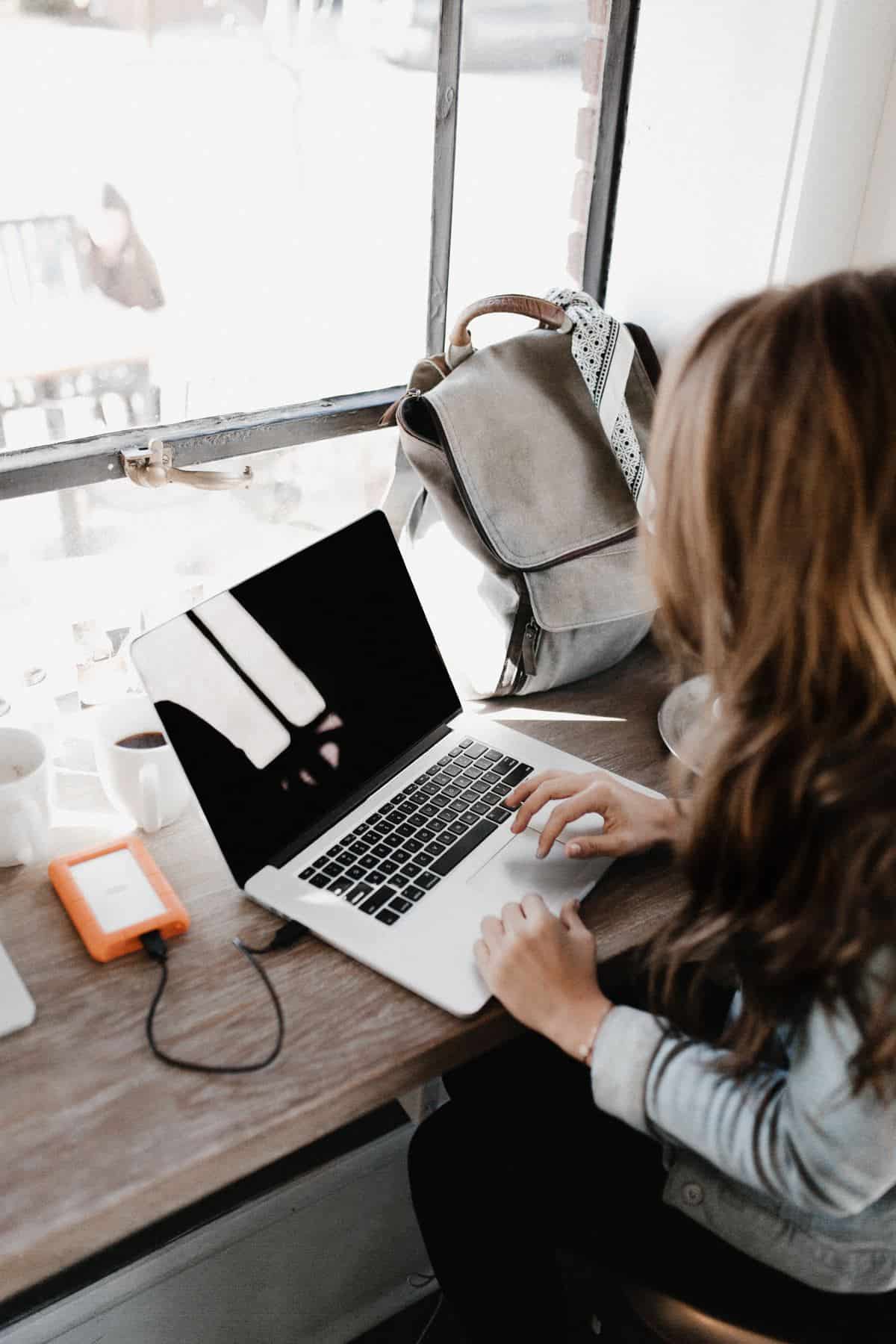 Brunette woman working on laptop. You can enroll online. Currently, there is no fee to enroll on the government site, but they will start charging a fee. #EVUS #visittheUS #traveltips #travel