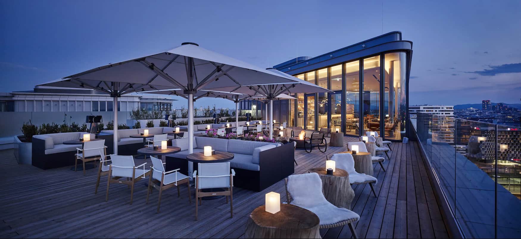 deck chairs and umbrellas on hotel rooftop at dusk overlooking city