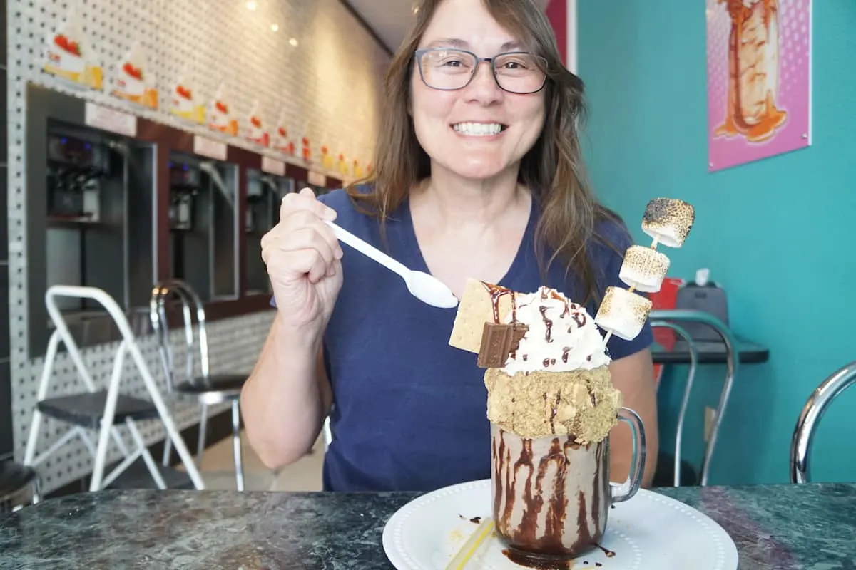 woman with brown hair and glasses enjoying a s'mores monster shake 