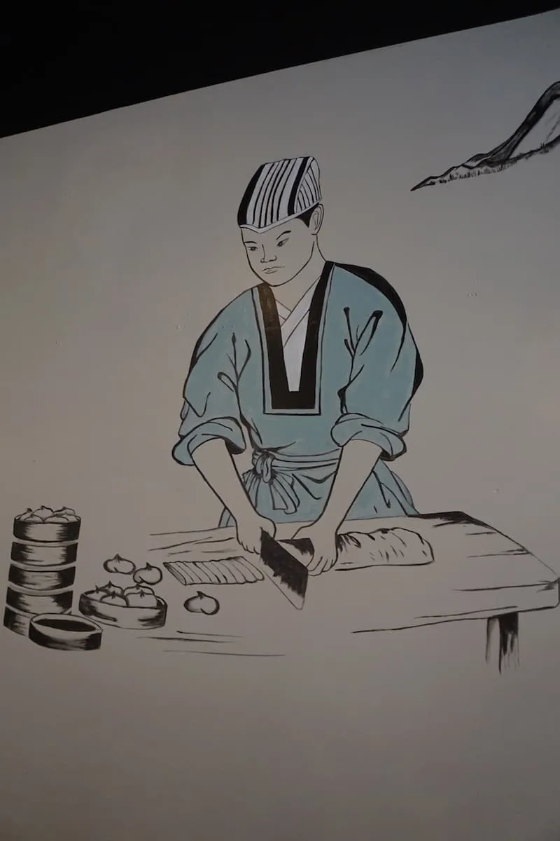 black and white mural of Japanese chef in teal coat making dumplings