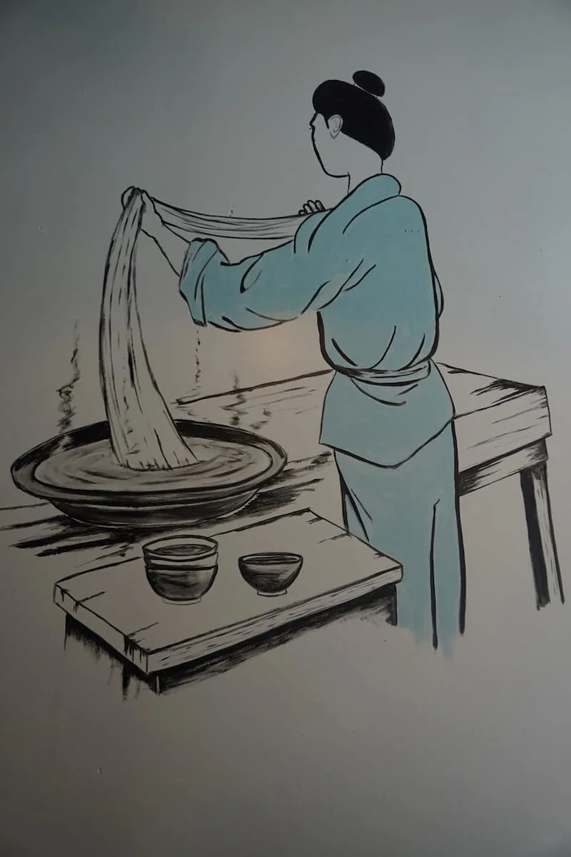 black and white mural of Japanese chef in teal coat making ramen