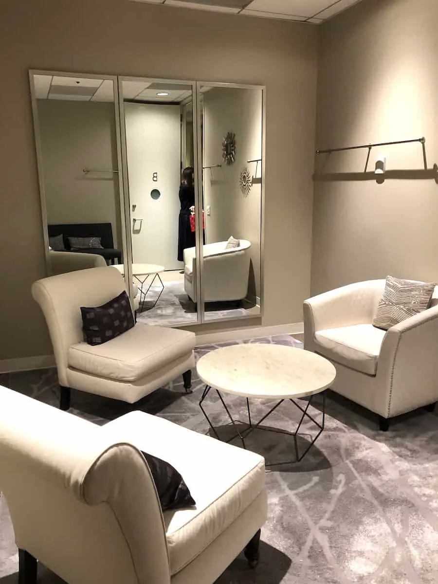 access suite lounge stylist room with three white leather chairs and clothes rod on wall