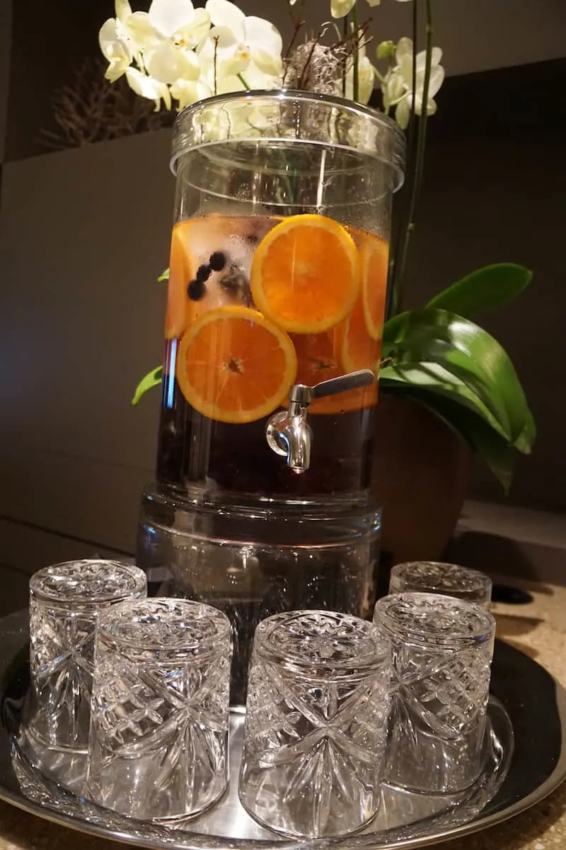 Clear jar of water with orange slices and blueberrys and crystal drinking glasses at access suite lounge