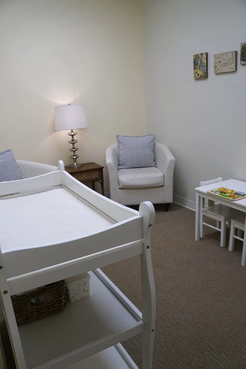 room in the south coast plaza access lounge with white changing table, two white leather chairs, a small white childrens desk and chairs