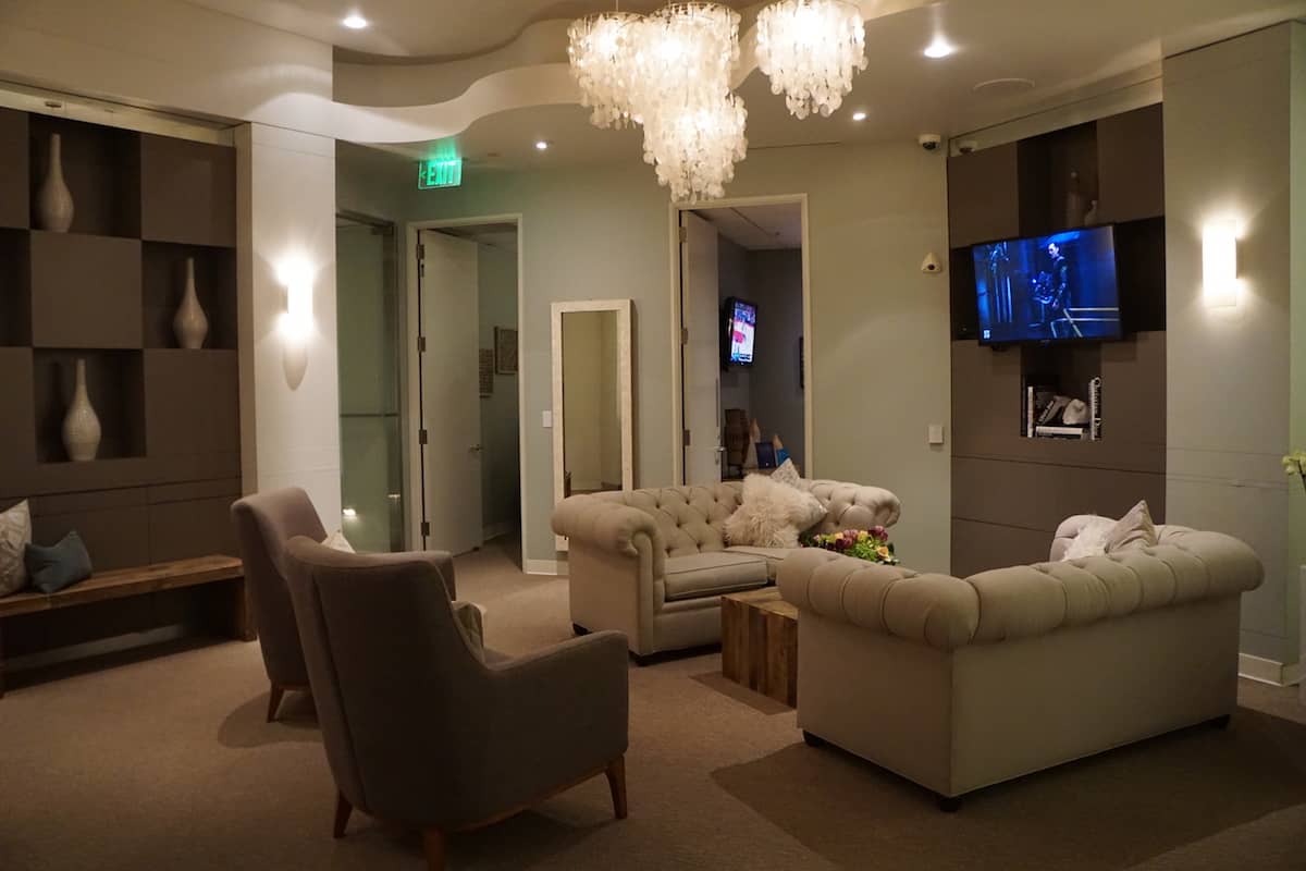 two plush neutral colored loveseats with decorative pillows, two padded chairs, a wood coffee, and wall-mounted TV