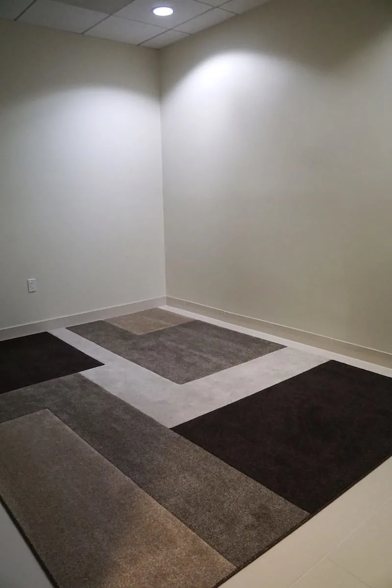 empty tiled room with beige walls and a carpet with different shades of brown blocks