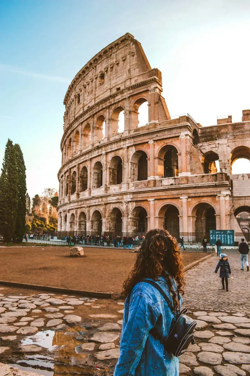 woman with long curly dark hair wearing blue jean jacket standing near Colosseum, Rome