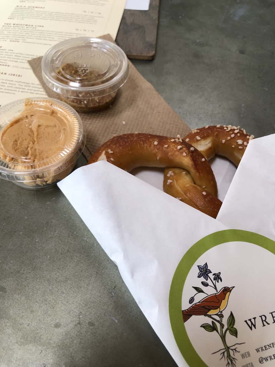 soft pretzel in paper sleeve with orange beer cheese and grainy mustard