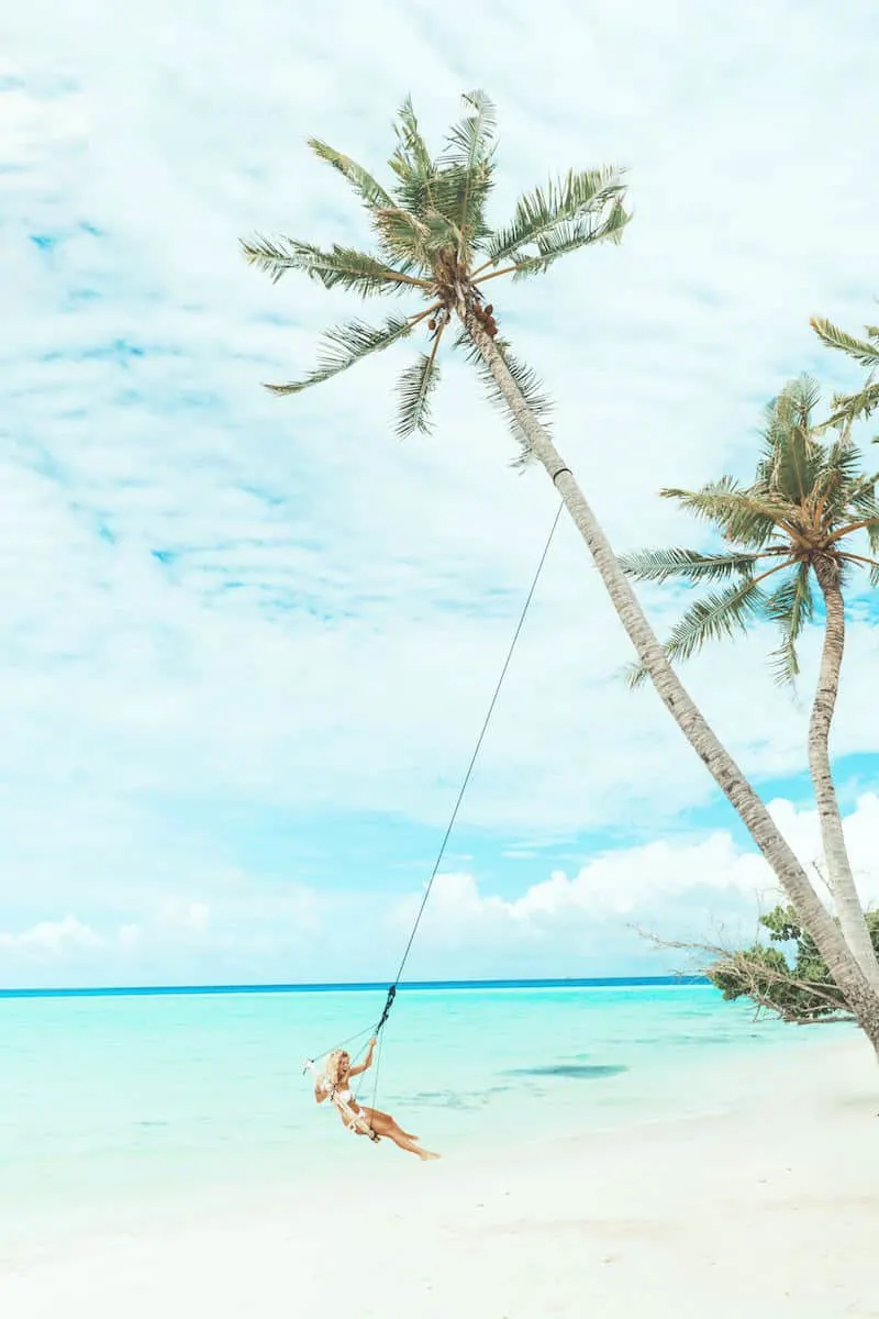 young blonde woman on beach palm tree swing