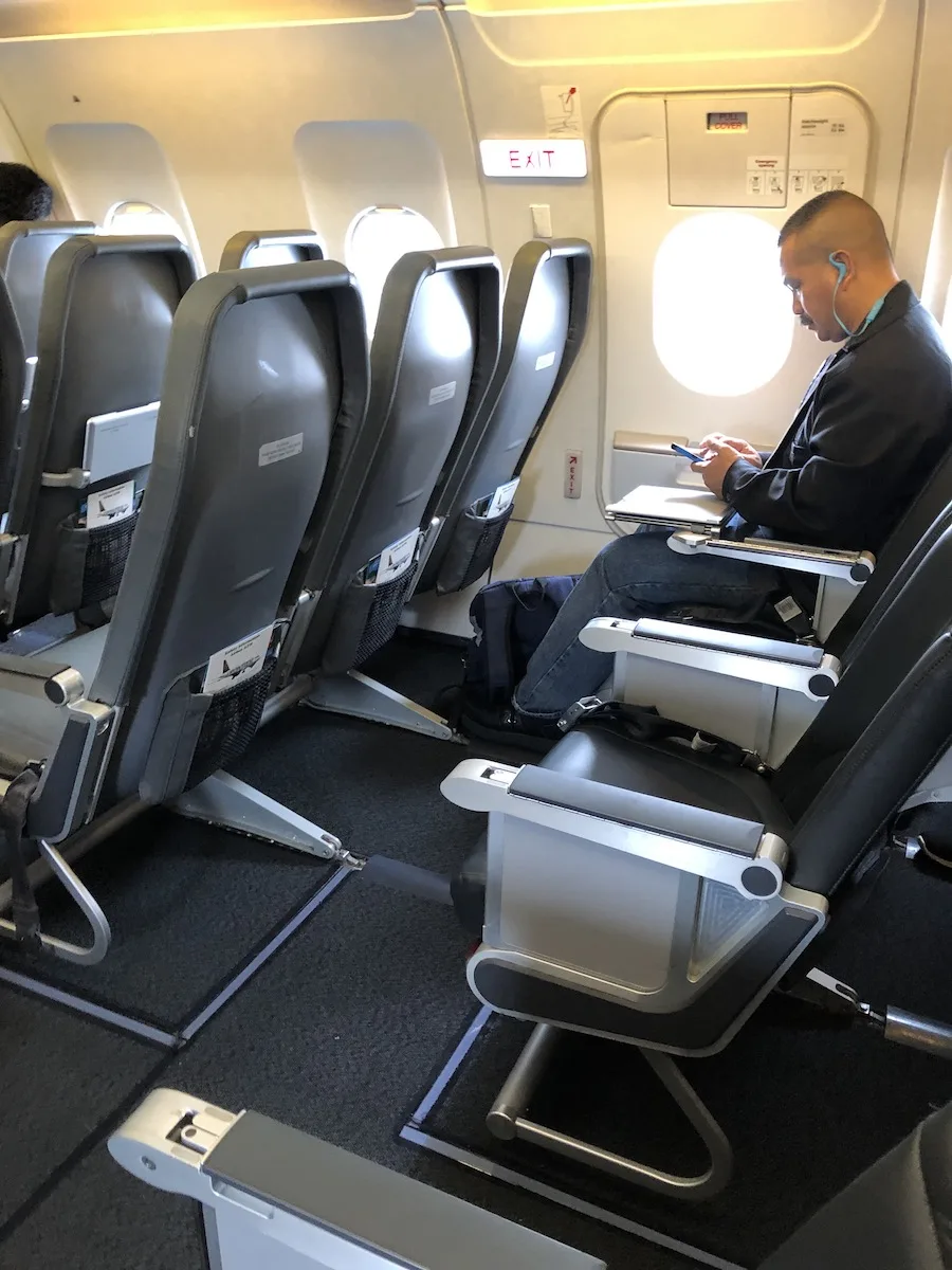 man sitting in window seat in exit row on airplane