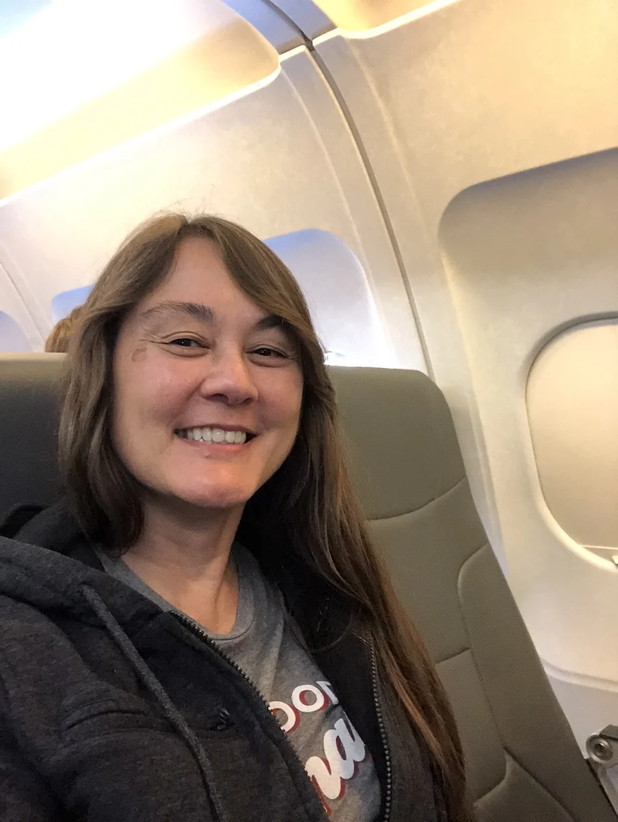 smiling woman with dark hair sitting in the middle seat of an airplane