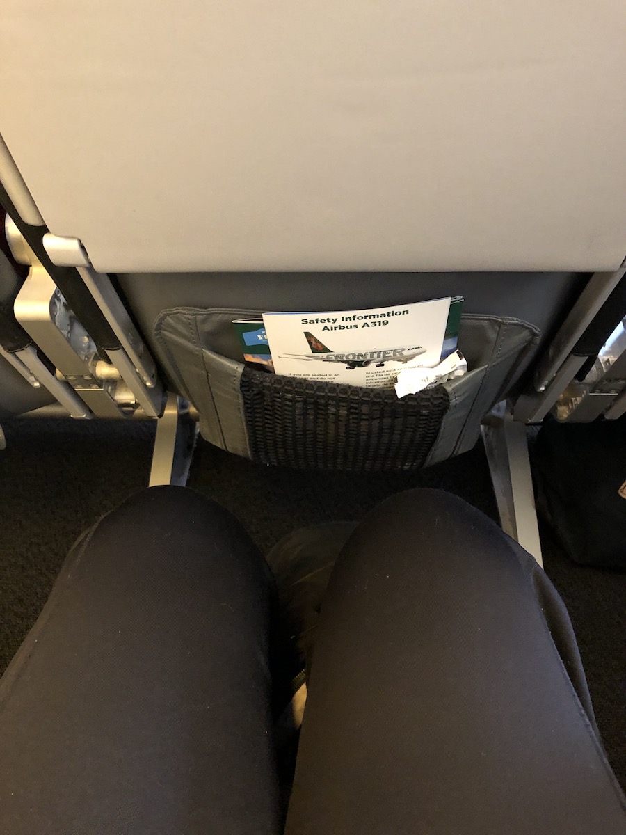 legs of woman wearing black pants sitting in an airline seat with decent leg room