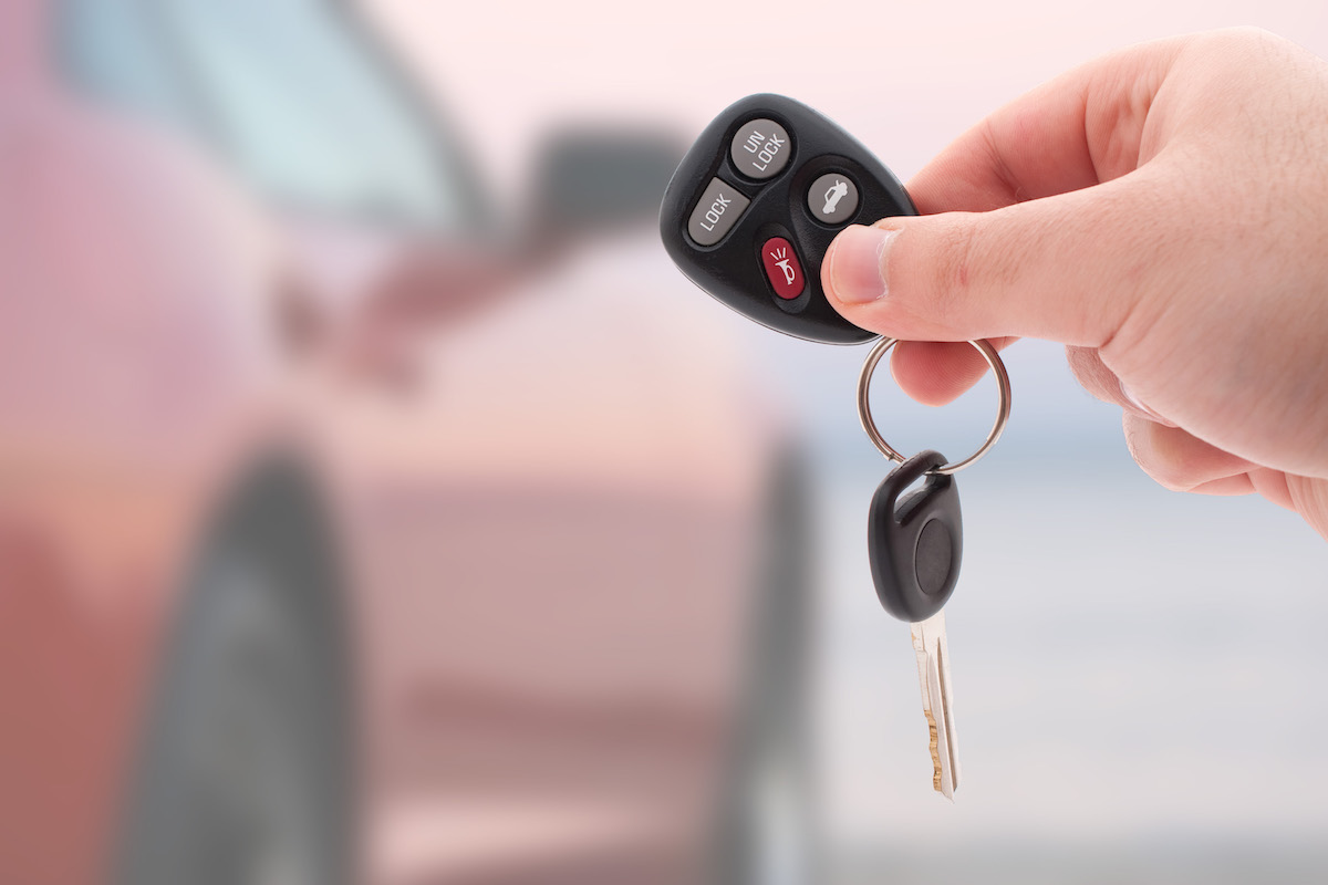 A hand holding car keys and a remote control for keyless entry isolated over white.