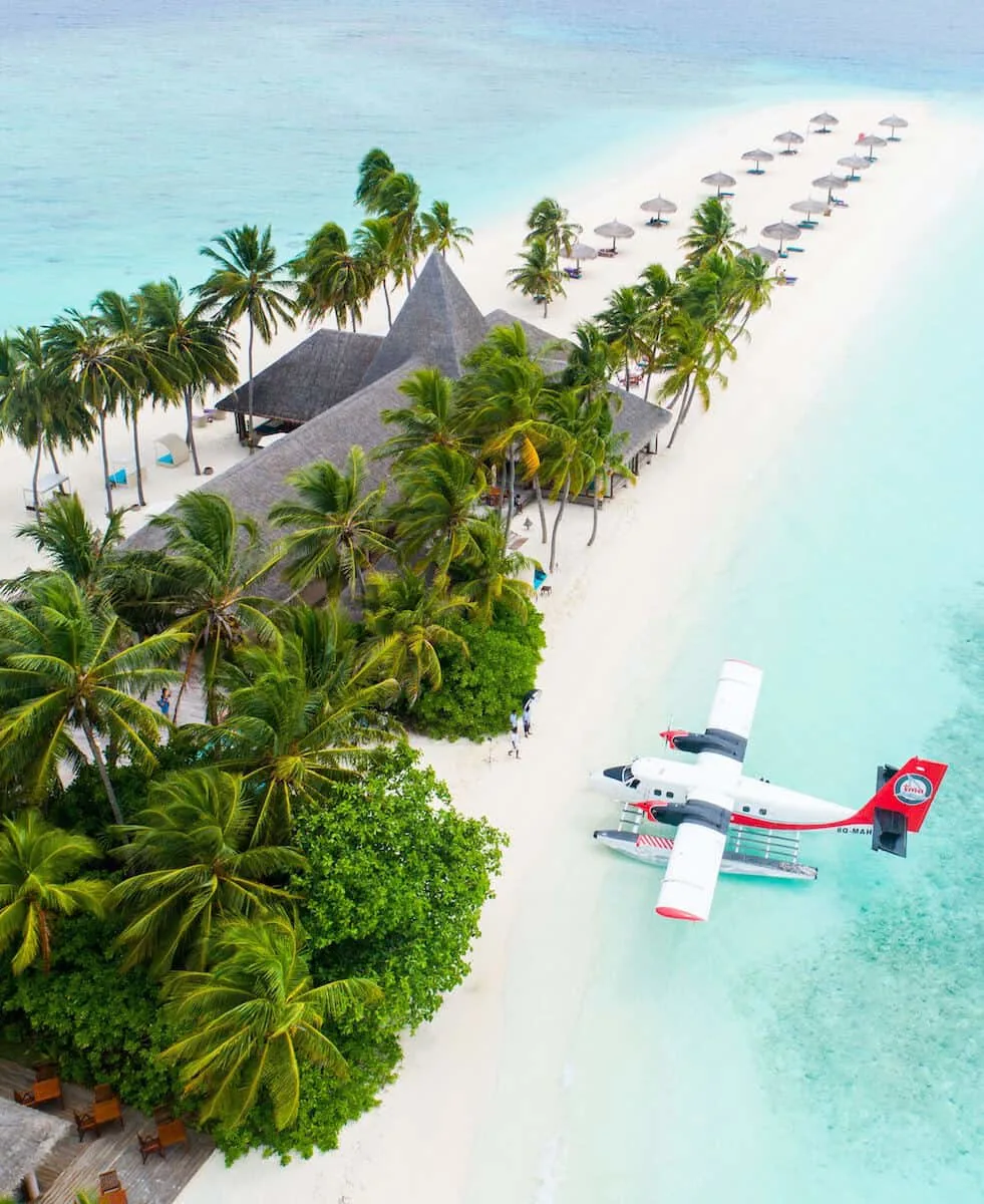 red and white small plane flying over beach front tropical resort