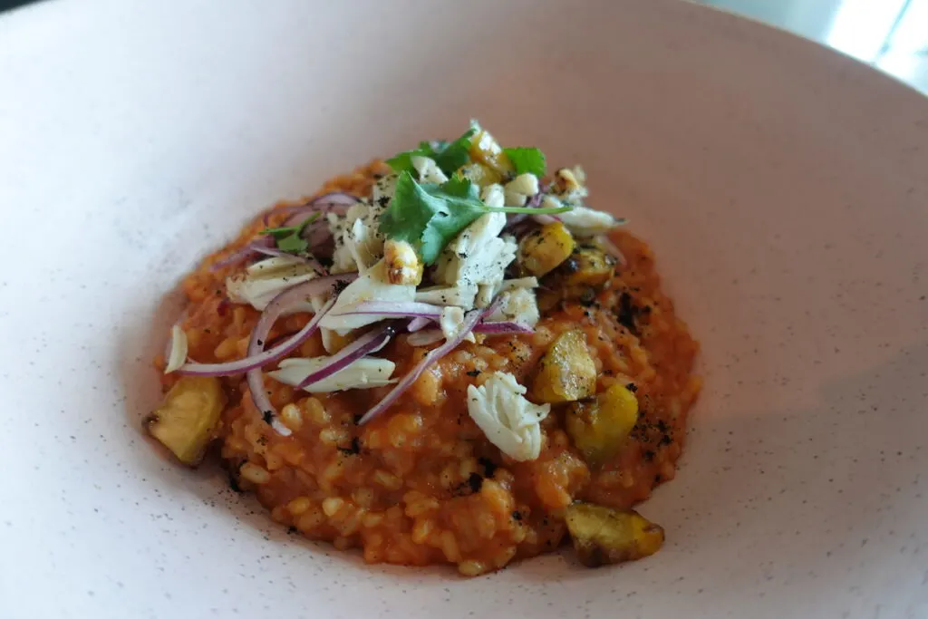 red risotto topped with pieces of crab in white bowl