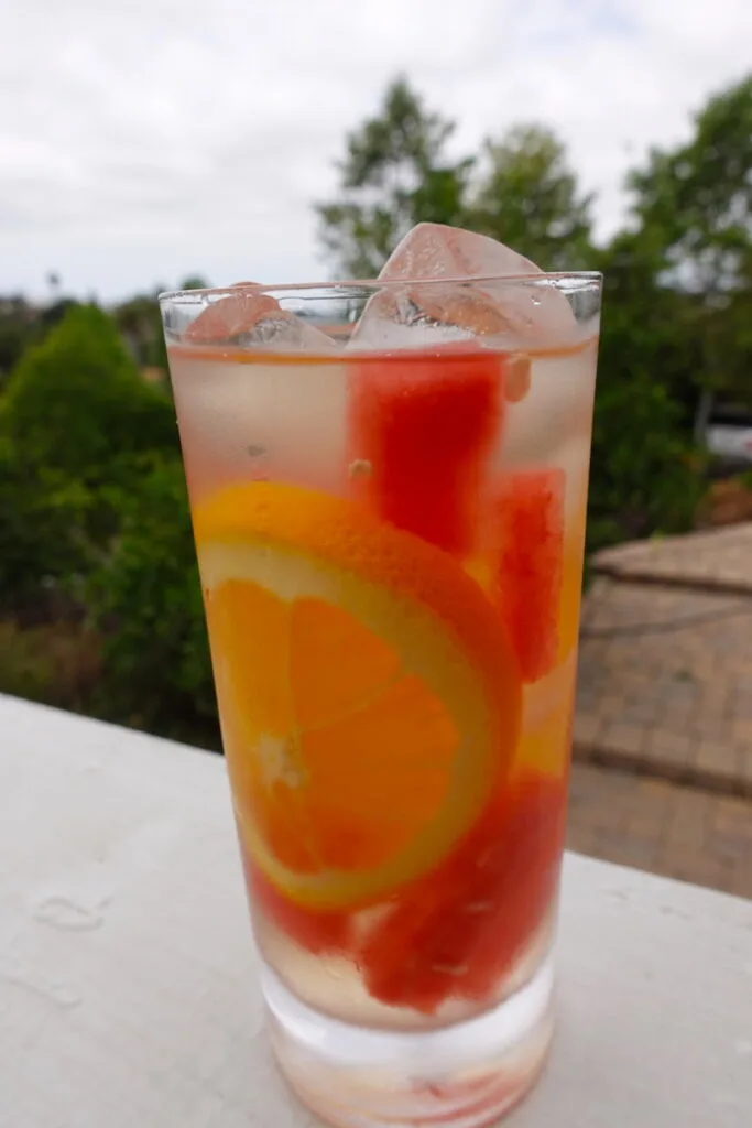 whiskey, coconut water, watermelon chunks, and orange slices in highball glass for World Whiskey Day