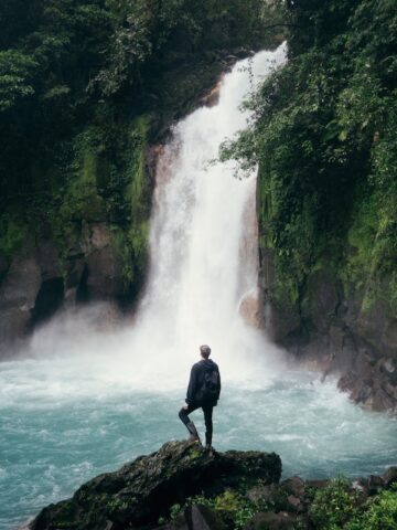 man standing on cliff near falls