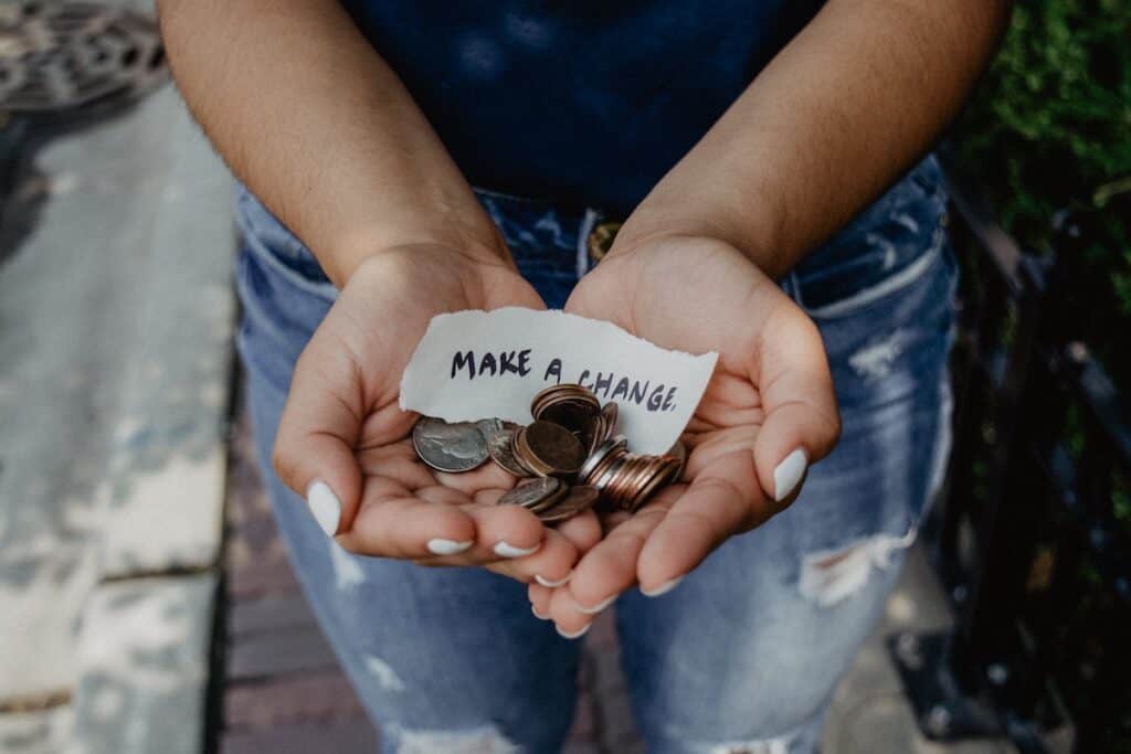 person showing both hands with make a change note and coins; earn miles and points without a credit card with charitable donations