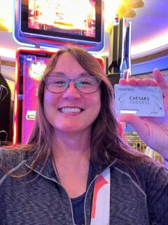 smiling brunette woman standing in front of a slot maching holding casino players card