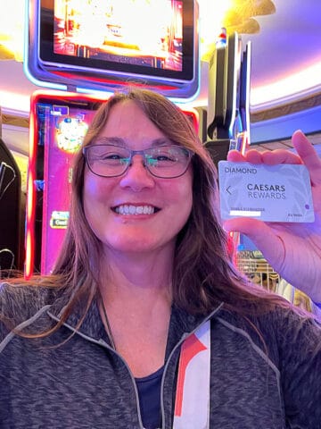 smiling brunette woman standing in front of a slot maching holding casino players card