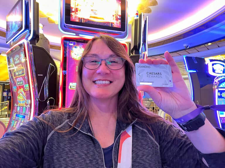 smiling brunette woman standing in front of a slot maching holding casino players card