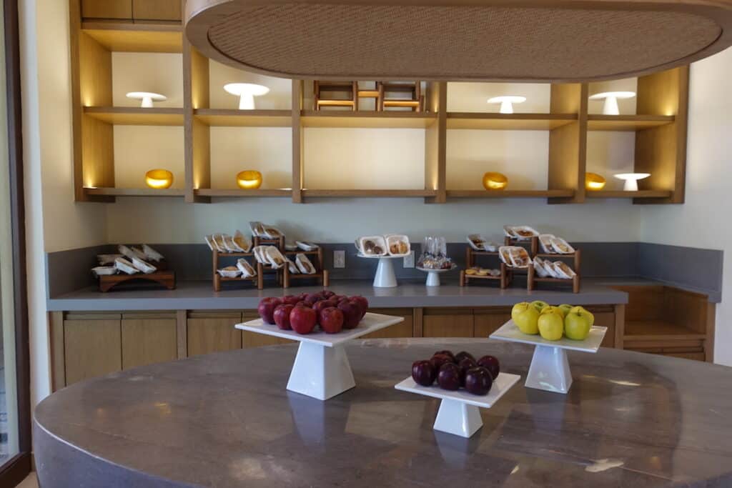 red and yellow green apples on white stands, plums on white stands, packaged snacks and sandwiches in room