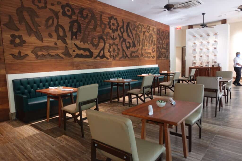 beige leather chairs brown wood tables, and long emerald green leather booth in hotel restaurant with flower etched wood wall