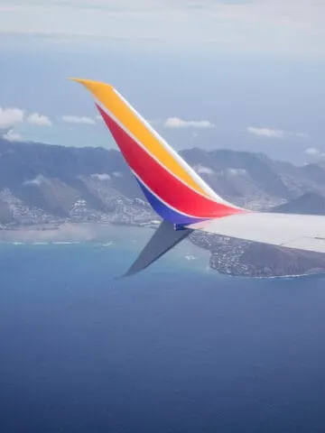airplane tail painted yellow, red, and blue flying over tropical island