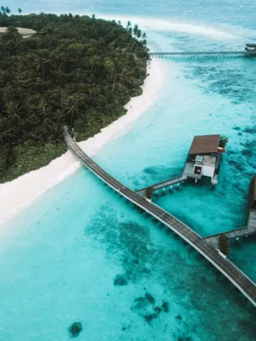 wood paths leading from white sand beach lush tropical island to overwater bungalows in turquoise green water