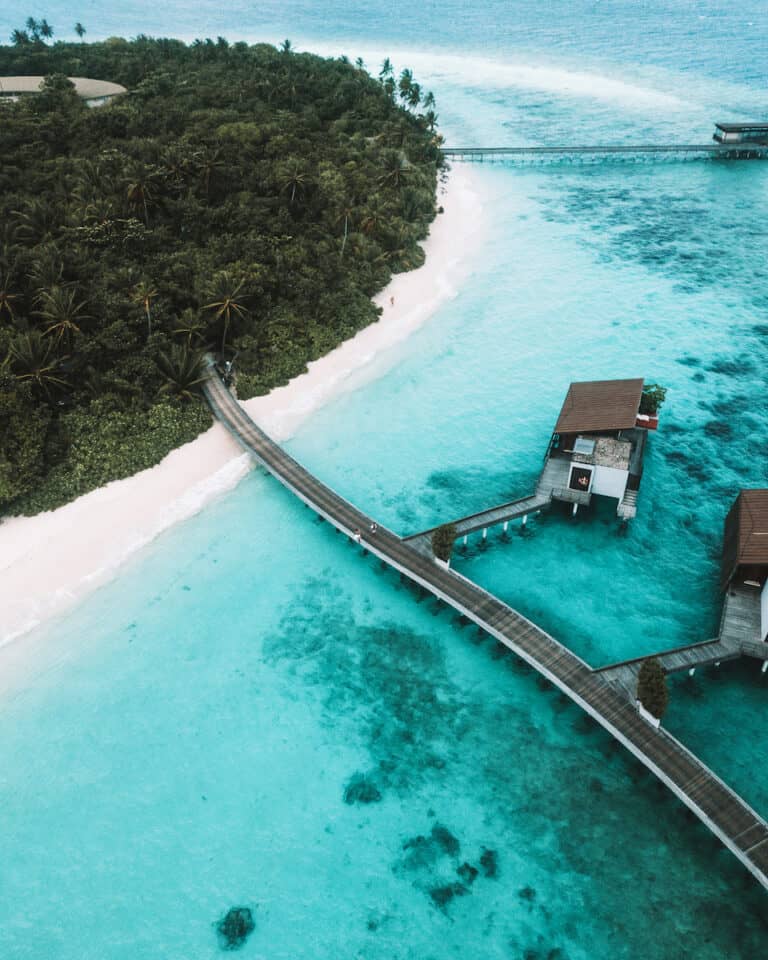 wood paths leading from white sand beach lush tropical island to overwater bungalows in turquoise green water