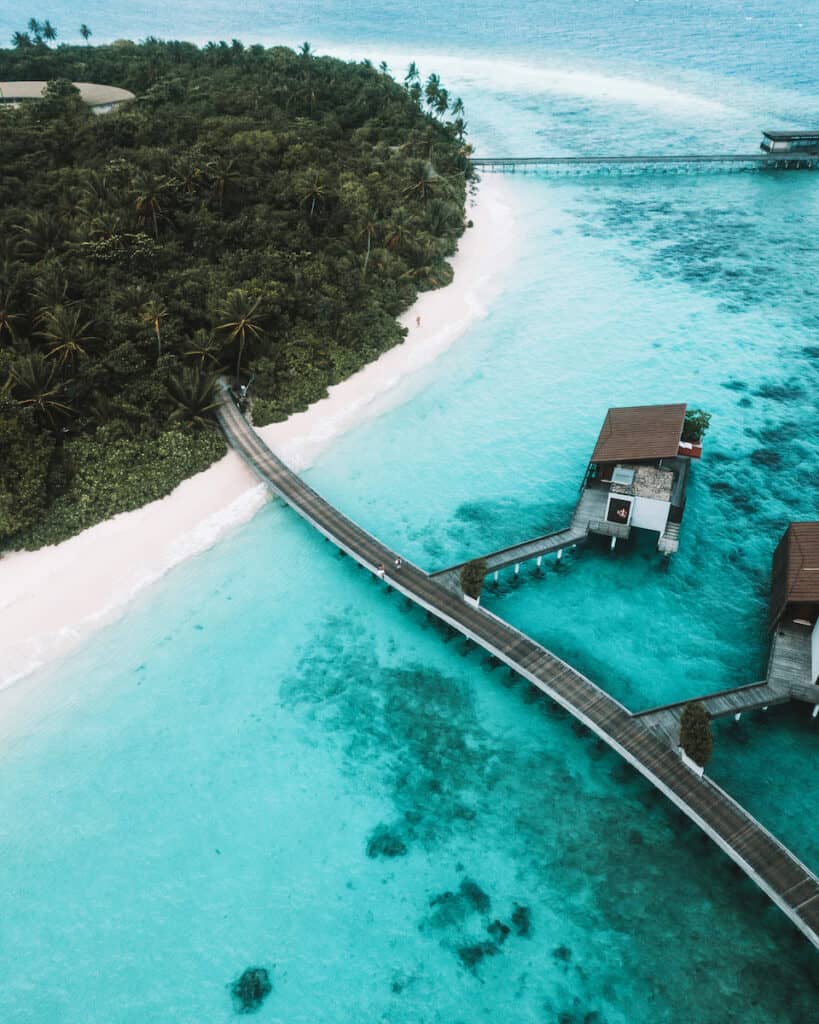 wood paths leading from white sand beach lush tropical island to overwater bungalows in turquoise green water