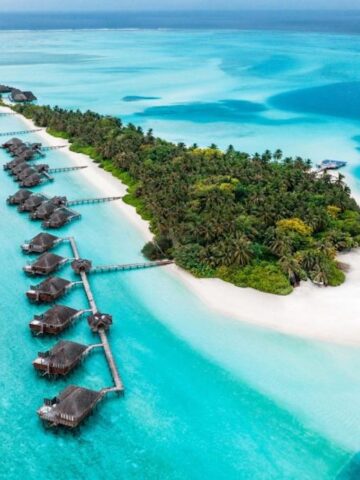 lush green tropical island with overwater villas surrounded by turquoise green and azure blue water