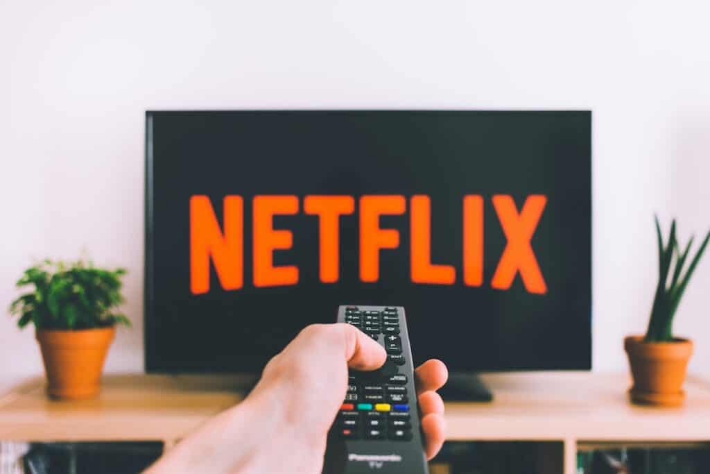 person holding remote pointing at TV on wood table showing netflix title on screen