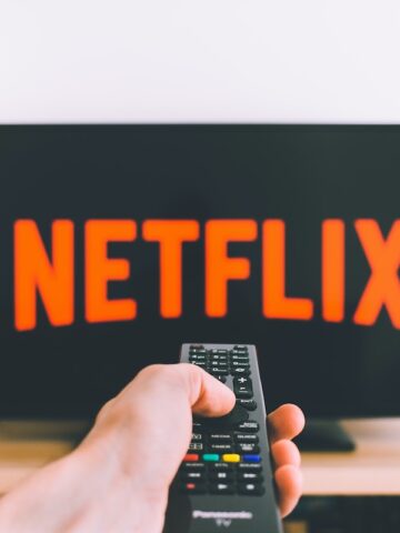 person holding remote pointing at TV on wood table showing netflix title on screen