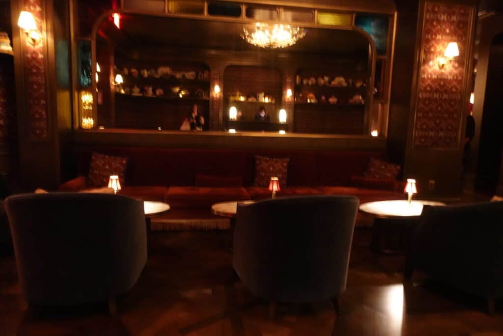 red velvet booths and dark green velvet chairs in front of large picture mirror in dimly lit room