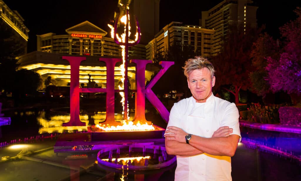 blonde haired caucasian male in chef jacket standing with arms crossed in front of burned HK sign at Caesars Palace, chef Gordon Ramsey Hells Kitchen