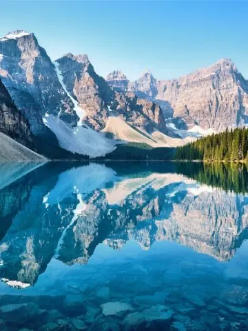 snow covered mountains and tall dark green trees reflected in crystal clear lake, scenery of mountain, Moraine Lake, Banff, Canada