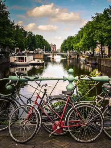 assorted color bicycles parked next to pastel green metal rails next to river in Amsterdam Netherlands