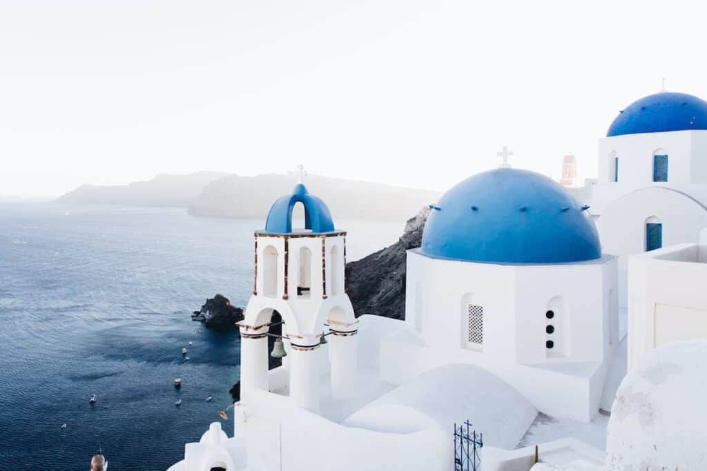 stark white buildings with blue round domed roofs sitting on cliffside overlooking the ocean in Santorini, Greece