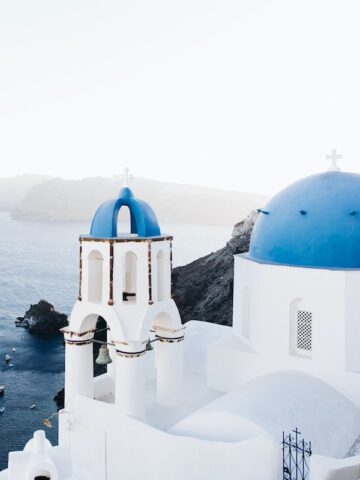 stark white buildings with blue round domed roofs sitting on cliffside overlooking the ocean in Santorini, Greece