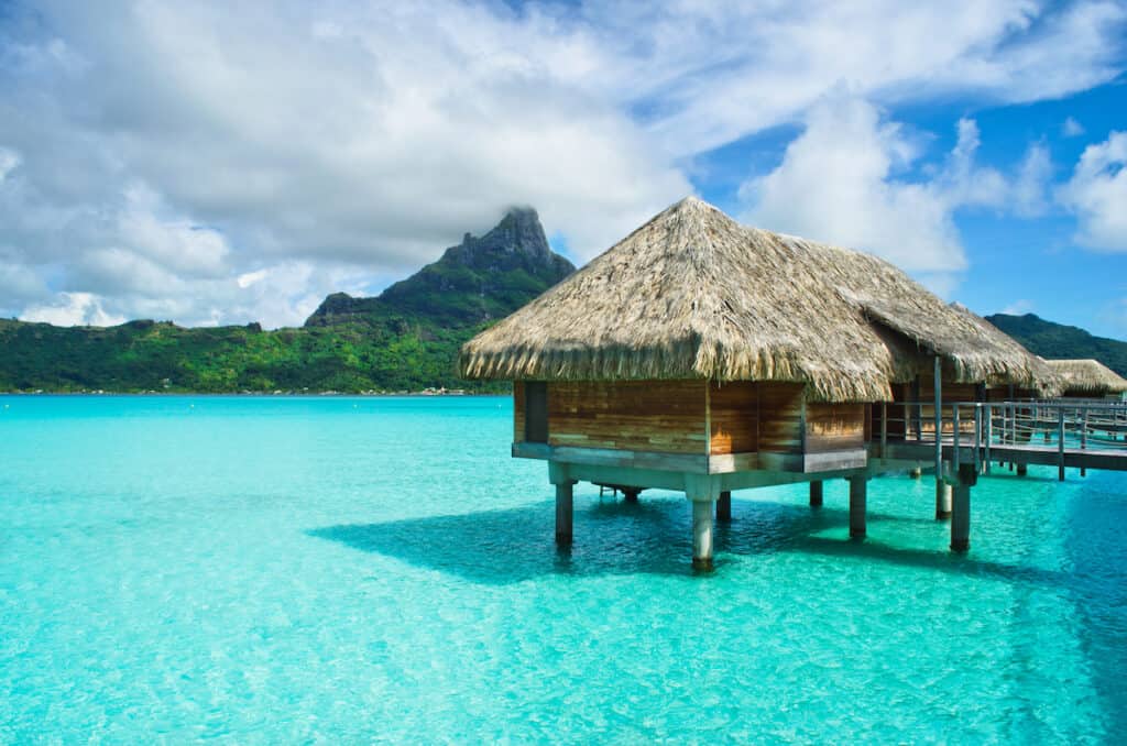 Luxury overwater thatched roof bungalow in a honeymoon vacation resort in the clear blue lagoon with a view on the tropical island of Bora Bora, near Tahiti, in French Polynesia.