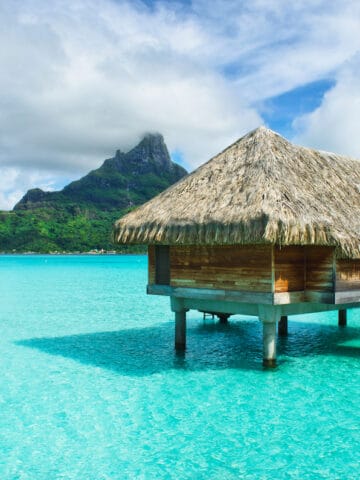 Luxury overwater thatched roof bungalow in a honeymoon vacation resort in the clear blue lagoon with a view on the tropical island of Bora Bora, near Tahiti, in French Polynesia.