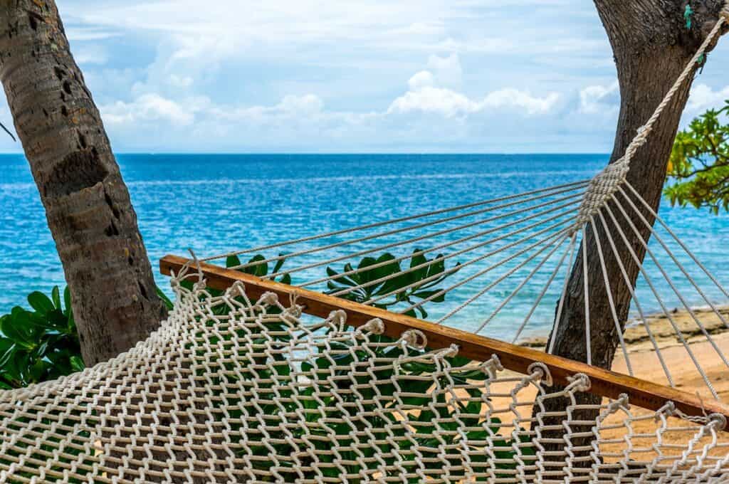 white hammock tied on tree on beach overlooking crystal blue water Malolo Island Fiji