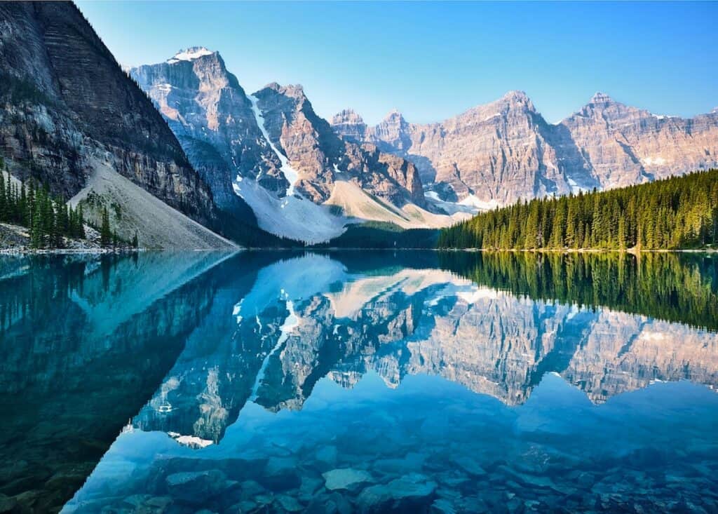 brown snow covered mountains and dark freen tall trees behind crystal clear mirror lake reflecting image on lake surface, scenery of mountain, moraine lake canada