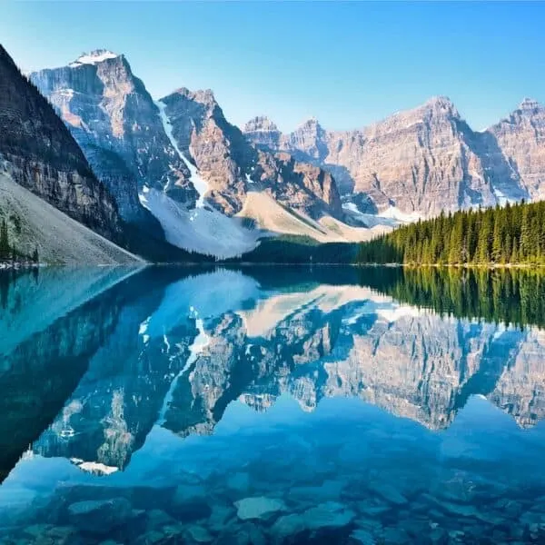 brown snow covered mountains and dark freen tall trees behind crystal clear mirror lake reflecting image on lake surface, scenery of mountain, moraine lake canada