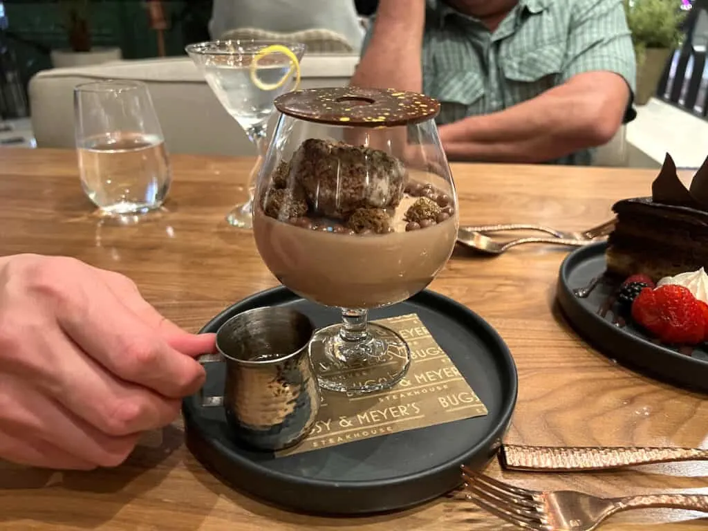 small cake on top of chocolate mousse in brandy glass topped with chocolate disk served on black round plate